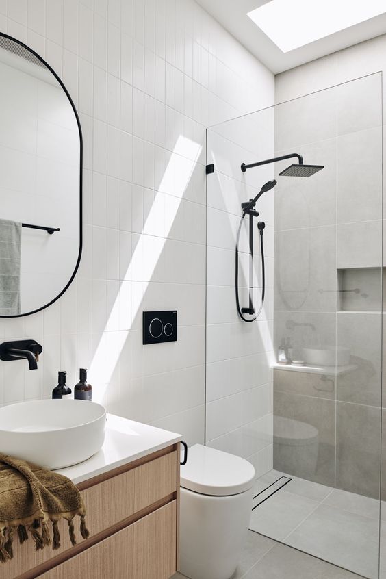 a contemporary bathroom clad with white skinny tiles, with a neutral vanity, a walk in shower with black fixtures and a niche for storage