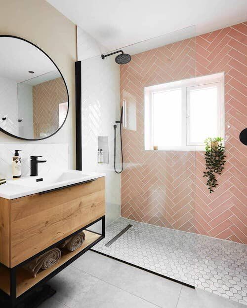a contemporary bathroom with pink herringbone tiles and marble ones in the walk-in shower plus black fixtures