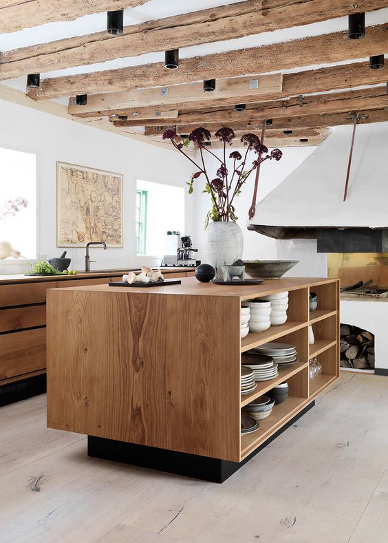 a contemporary kitchen with stained sleek cabinets, a matching kitchen island with open shelves and rough wooden beams and a hearth