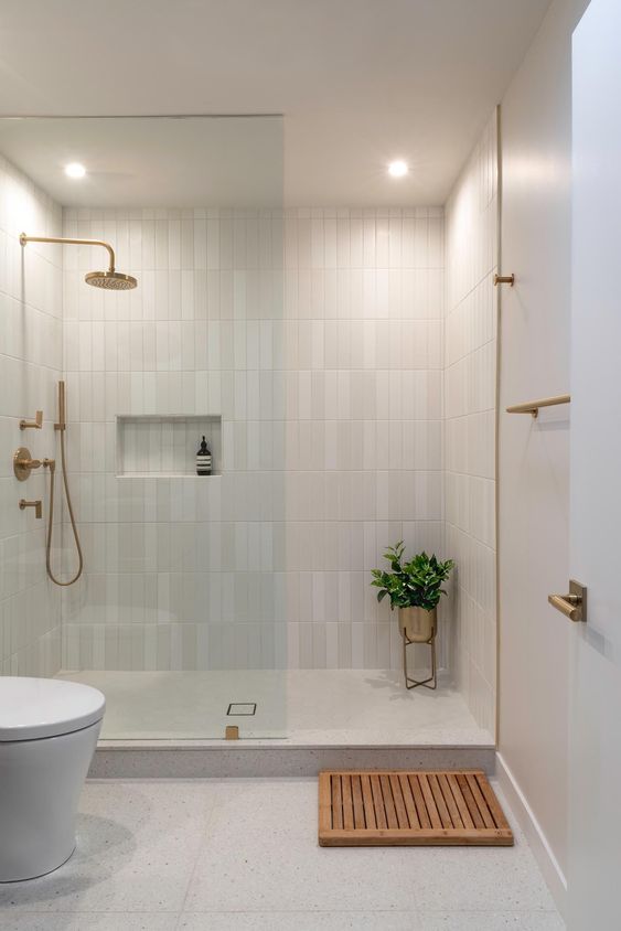 a contemporary neutral bathroom with skinny tiles and a terrazzo floor, a walk-in shower and brass fixtures for more elegance
