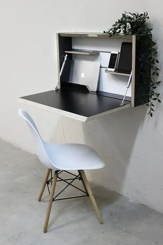 a cool small working space with a black Murphy desk with a potted plant and all the gadgets, a simple white chair