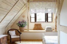 a cozy cabin bedroom with blonde wood on the walls, ceiling and floor, with vintage cottage furniture, blooms in a basket and a lace curtain