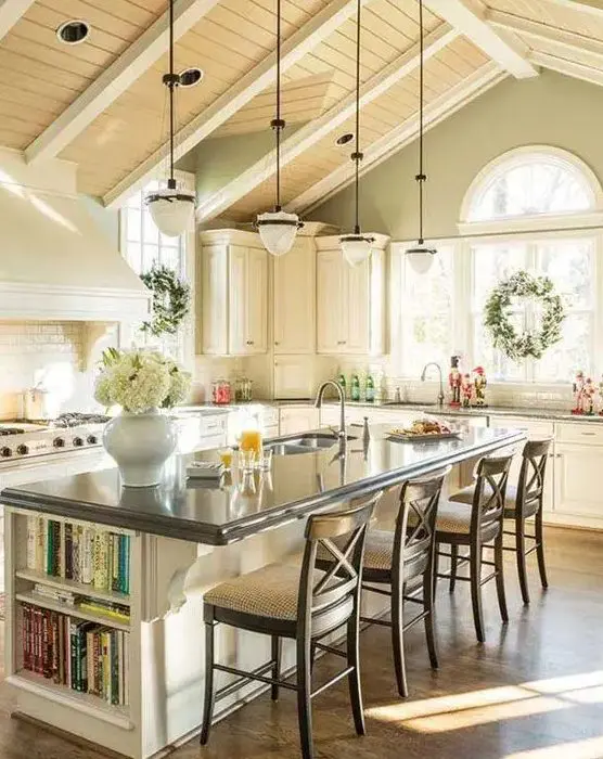 a cozy farmhouse kitchen with green walls, a light stained ceiling, a white subway tile backsplash, a large kitchen island with a black countertop and built-in open bookshelves