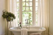 a gorgeous neutral bathroom in French chic style, with a vintage touch, an oval tub, a vintage stool and a view of the garden