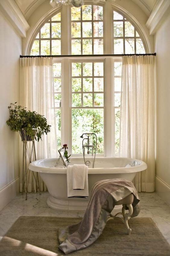 a gorgeous neutral bathroom in French chic style, with a vintage touch, an oval tub, a vintage stool and a view of the garden