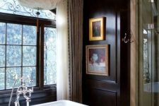 a gorgeous vintage bathroom with black walls, a vintage tub, a gorgeous chandelier and artworks