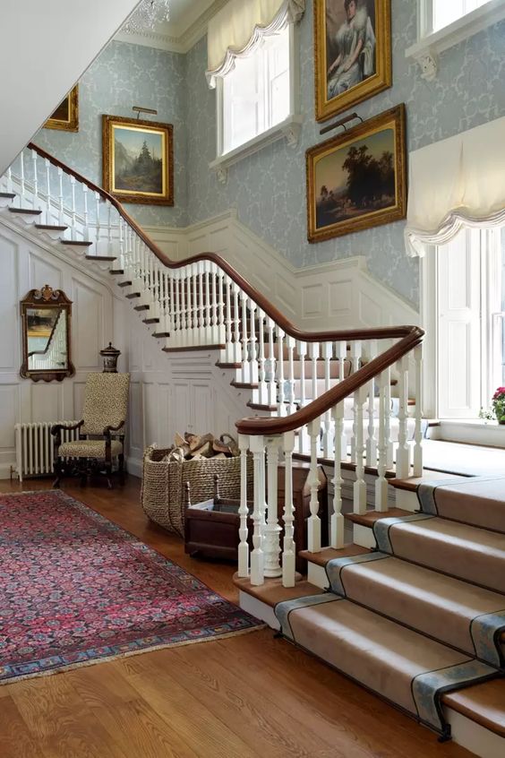 a historic house with light-stained floors, dark-stained railing, white paneling, lots of refined vintage artworks