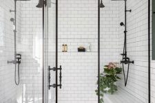 a large and chic walk-in shower clad with white and black and white tiles, with glass doors and vintage-inspired black fixtures