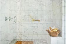 a large walk-in shower space clad with white marble tiles, with a built-in shelf and bench and a wooden mat