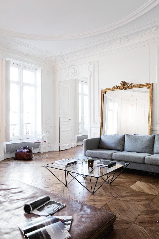 a light filled and airy French chic living room with a grey sofa, a leather daybed and a table with geometric legs