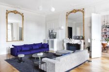 a lovely modern Parisian living room with an antique fireplace, a bold purple and grey sofa, a bench and some table and a couple of mirrors