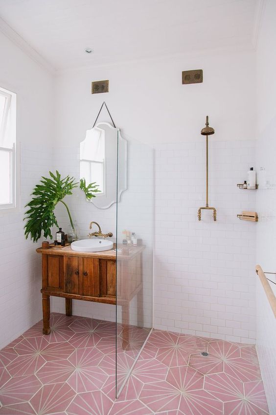 a lovely modern bathroom with white subway tiles and a pink geo tile floor, a walk-in shower with a glass partition, a stained wood desk