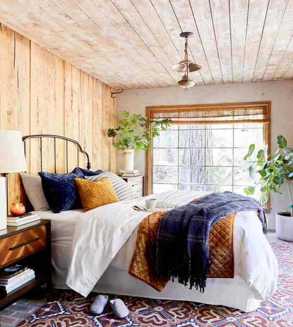 a lovely rustic bedroom with wooden walls and a ceiling, a metal bed with bright bedding, modenr dressers as nightstands and a vintage lamp