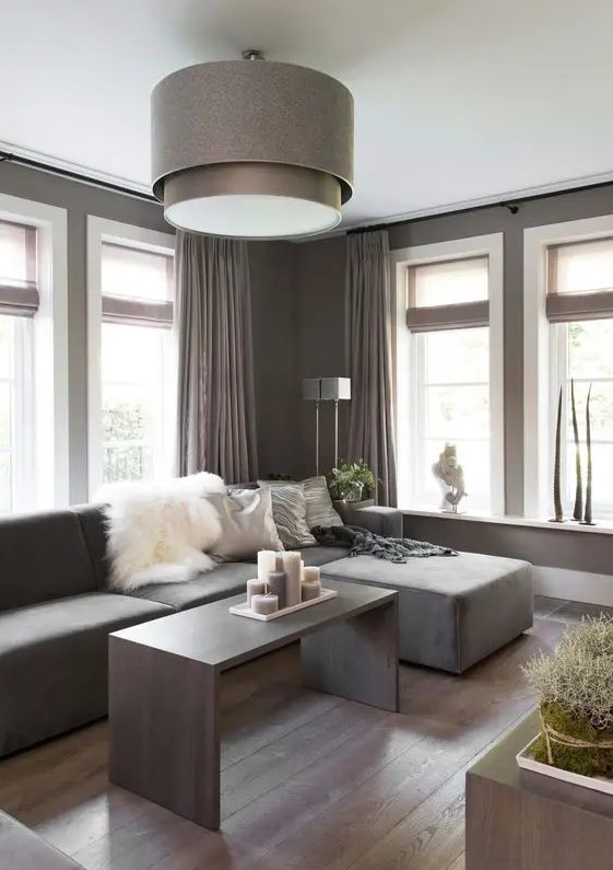 a lovely taupe contemporary living room with a matching low sofa, taupe curtains, a taupe coffee table with lots of candles and a taupe pendant lamp