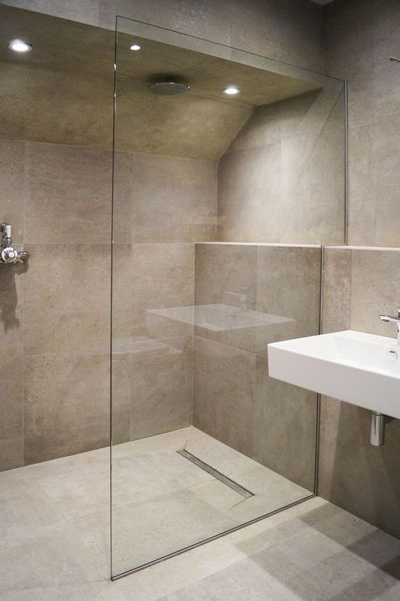 a minimalist bathroom with tan large-scale tiles, a walk-in shower with a glass partition, a wall-mounted sink
