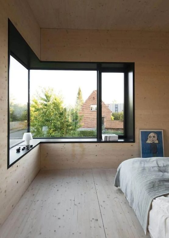 a minimalist bedroom clad with blonde wood, with a lovely view, contemporary furniture and a windowsill seat