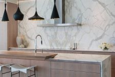 a minimalist kitchen with light-stained cabinets and white marble countertops, a marble backsplash, a large kitchen island with lots of drawers for storage