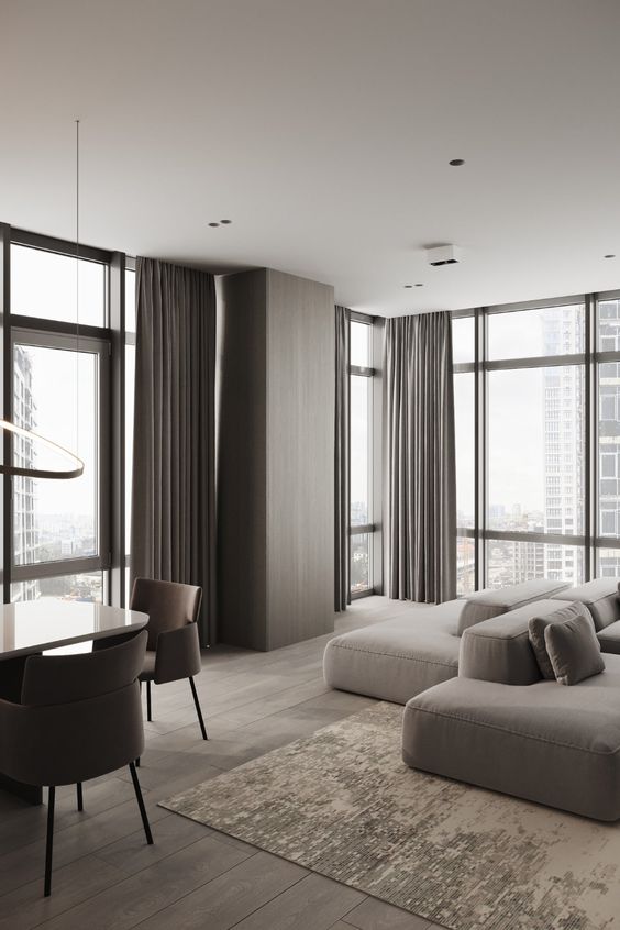 a minimalist taupe living room with floor-to-ceiling windows, a greige low sofa, taupe curtains and a pretty tan rug