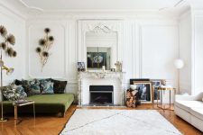 a modern French cic living room with an antique fireplace, a green sofa with printed pillows, a white one by the window and elegant touches of brass