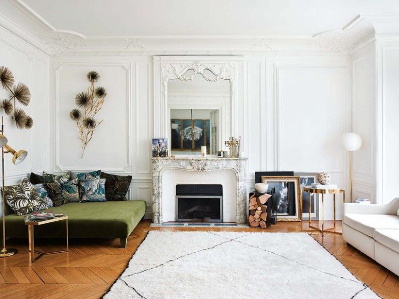 a modern French cic living room with an antique fireplace, a green sofa with printed pillows, a white one by the window and elegant touches of brass