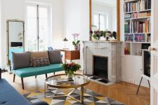 a modern and chic French living room with a marble fireplace, a bold turquoise loveseat and a navy sofa, mirrors and a glass coffee table