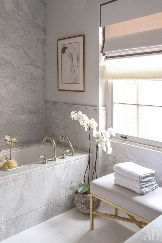 a modern and sophisticated French bathroom clad with white marble, a tub clad with it, too, a grey bench and a potted orchid is wow