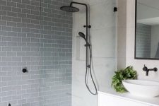 a modern bathroom with neutral and slate grey tiles in the walk-in shower, with black fixtures and some greenery