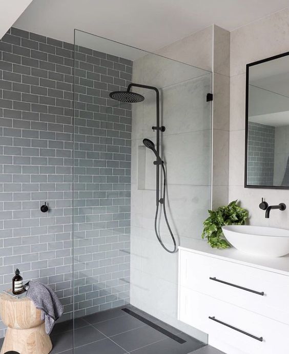 a modern bathroom with neutral and slate grey tiles in the walk-in shower, with black fixtures and some greenery