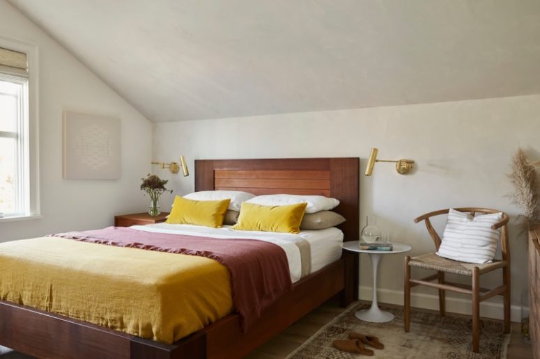 a modern bright bedroom wiht a stained bed and a matching nightstand, a white table as another nightstand and a woven chair