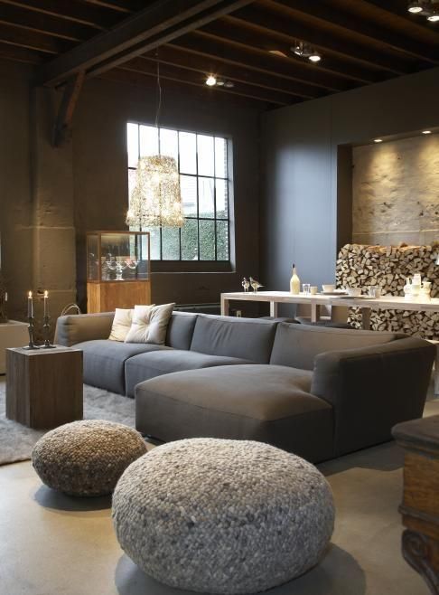 a modern chalet living room with taupe walls and wooden beams on the ceiling, a grey low sofa, pebble-like poufs and lights