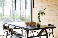 a modern dining room clad with blonde wood all over, with black furniture and lamps and a gorgeous natural view