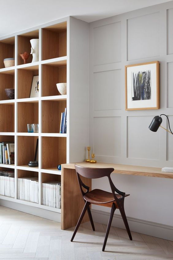 a modern dove grey home office with a large shelving unit, a stained desk, a dark stained chair and a blonde wood picture frame