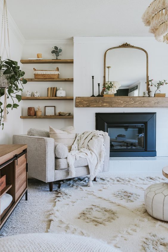 a modern neutral farmhouse living room with a wooden mantel, matching built-in shelves, a reddish console table and neutral textiles