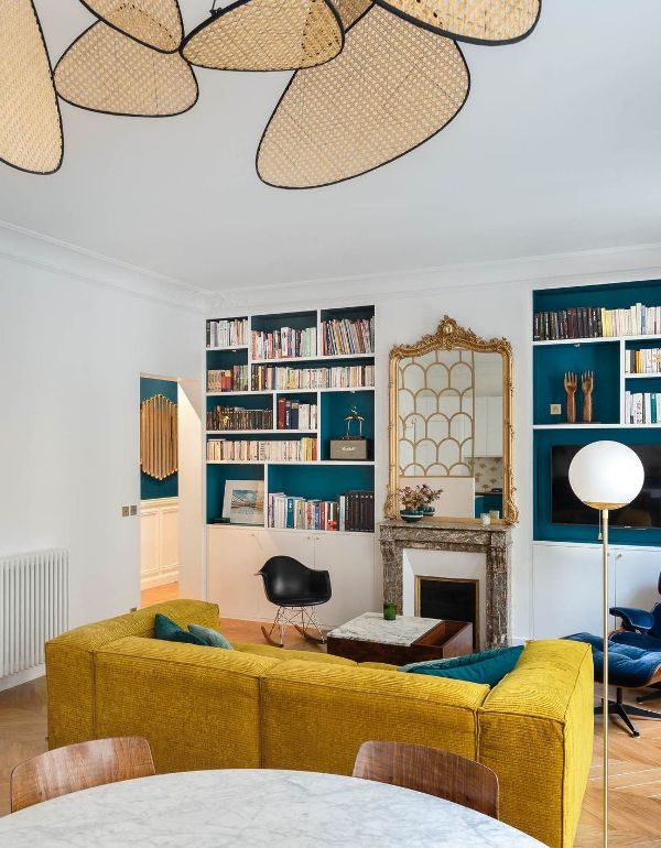 a modern to art deco living room in French style, with an antique fireplace, a mustard sofa, built-in bookcases and a mirror in an ornated frame