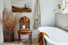 a neutral French bathroom with a grey tile wall, a herringbone floor, a clawfoot tub, a leather chair and dried branches in a basket