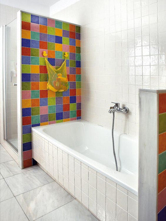 a neutral bathroom clad with square tiles and super bold multi color tile accents that mark the shower and the bathtub zone