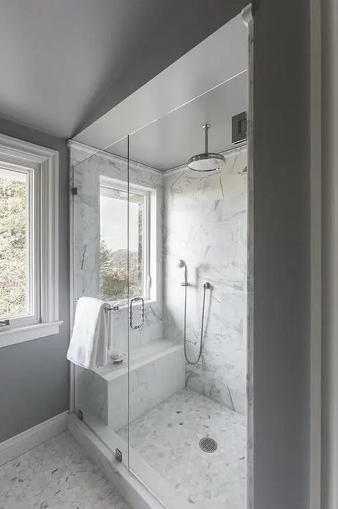 a neutral bathroom with grey walls, a white marble tile floor, a white marble shower space and penny tiles on the floor