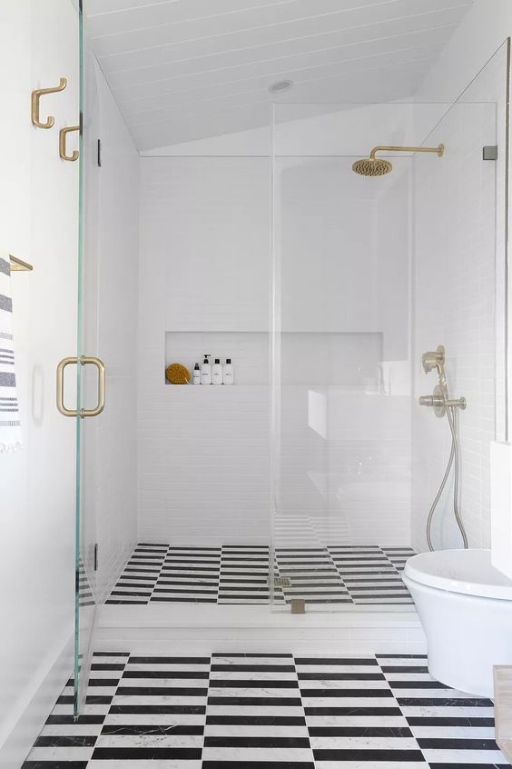 a pretty contemporary bathroom with white and black and white tiles, with white appliances, a walk-in shower and brass touches