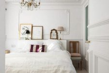 a pretty eclectic Parisian bedroom with a white bed with neutral bedding, stools and chairs, a crystal chandelier and a mini gallery wall