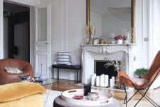 a pretty modern French chic living room with an antique fireplace, leather and velvet furniture of earthy tones and an oversized mirror