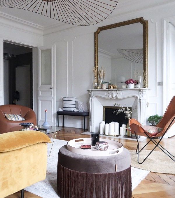 a pretty modern French chic living room with an antique fireplace, leather and velvet furniture of earthy tones and an oversized mirror