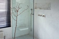 a refined and chic walk-in shower clad with white marble, with a single glass space divider and a built-in seat is a very seel and modern idea