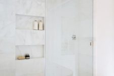 a refined contemporary bathroom with neutral tiles and a marble floor, niche shelves and neutral fixtures