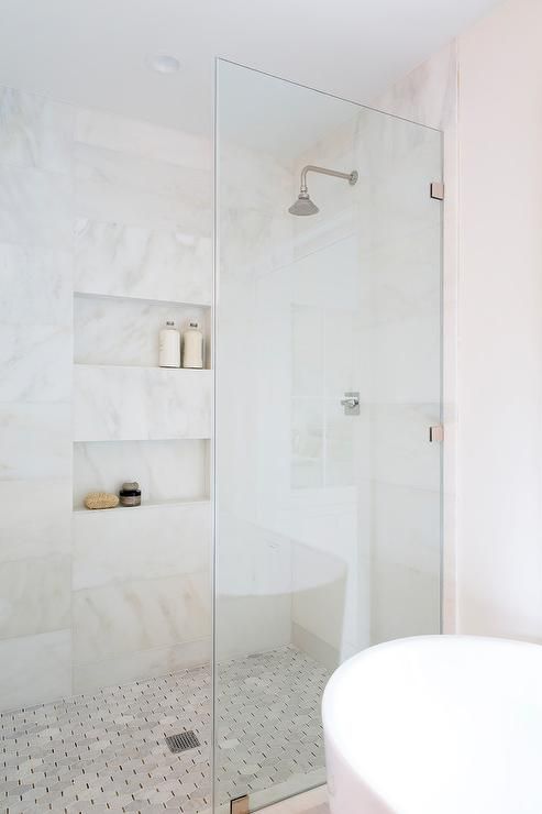 a refined contemporary bathroom with neutral tiles and a marble floor, niche shelves and neutral fixtures