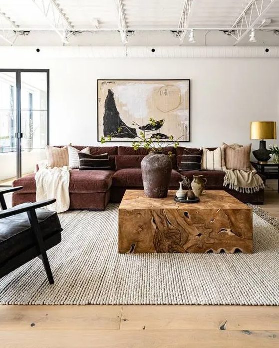 a refined living room with a burgundy sectional, a black chair, a light-stained wooden floor, a neutral rug and a rich-stained wooden table