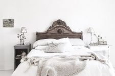 a refined vintage bedroom with a shabby chic wooden bed, neutrla bedding, a grey open storage nightstand and a shabby white table as a nightstand