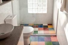a small and cool bathroom with white mini tiles and a bold and colorful tile floor, a white vanity with a concrete countertop, a bowl sink