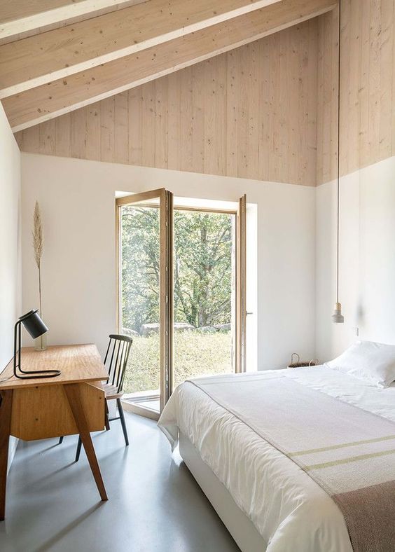 a small contemporary cabin bedroom with a blonde wooden ceiling and beams, simple mid-century modern furniture and an access to the garden