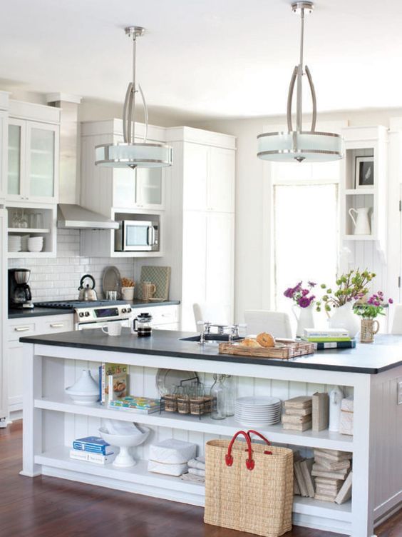 a small white kitchen with black countertops and a large kitchen island with large open shelves for storage is cool