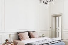 a sophisticated Parisian bedroom with neutral paneling, a bed with pastel bedding, mismatching nightstands and a crystal chandelier